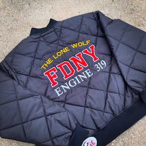 May include: Black quilted jacket with a red and white "FDNY Engine 319" embroidered on the back. The text "The Lone Wolf" is embroidered above the FDNY logo in yellow.