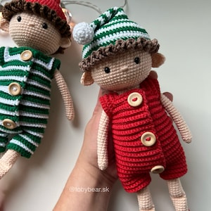 May include: Two crocheted elf dolls wearing pajamas. One doll is wearing green and white striped pajamas and a red hat with a white pom-pom. The other doll is wearing red pajamas and a green and white striped hat. Both dolls have brown yarn hair and brown eyes.