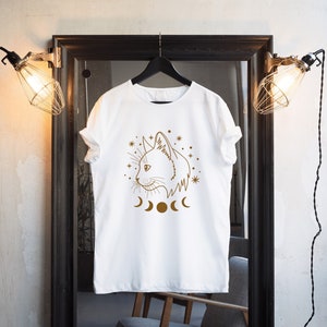 May include: White t-shirt with a brown line drawing of a cat's face with a crescent moon and stars around it.
