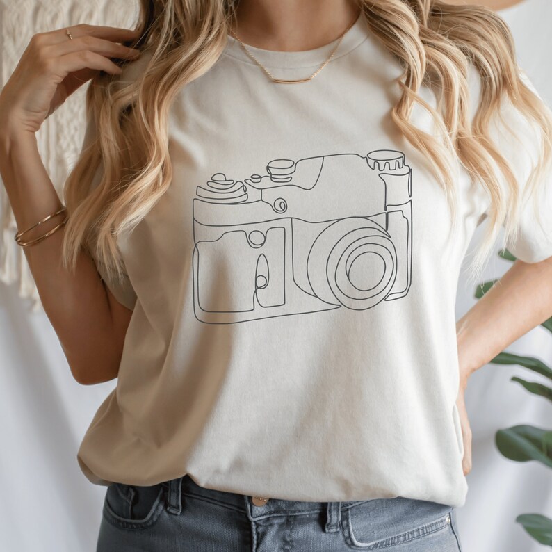 May include: A white t-shirt with a simple line drawing of a camera on the front.