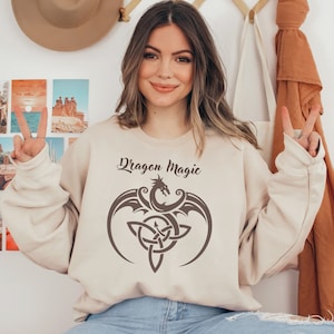 May include: A beige sweatshirt with a brown dragon and a Celtic knot design. The text "Dragon Magic" is printed on the sweatshirt.