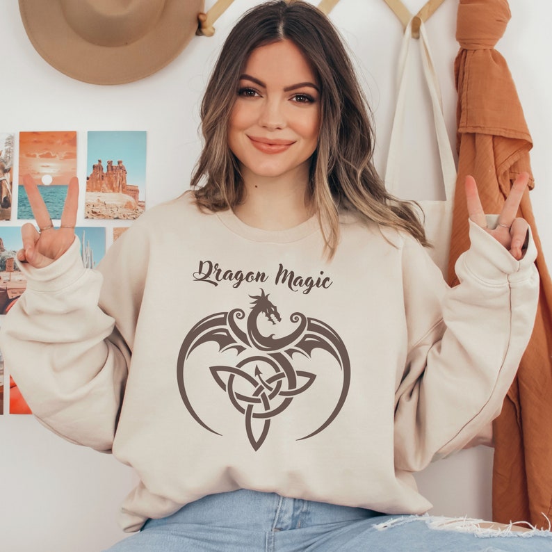 May include: A beige sweatshirt with a brown dragon and a Celtic knot design. The text "Dragon Magic" is printed on the sweatshirt.