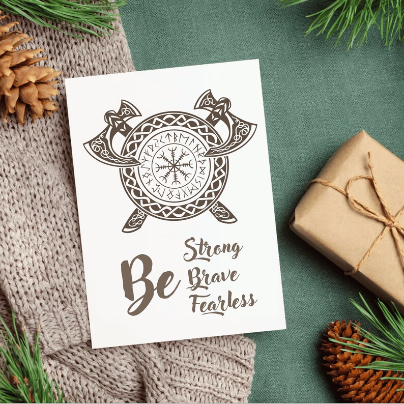 K&ouml;nnte beinhalten: Eine wei&szlig;e Karte mit einer braunen Illustration von zwei gekreuzten &Auml;xten und einem kreisf&ouml;rmigen Symbol mit Runen. Der Text "Be Strong Brave Fearless" steht unter der Illustration.