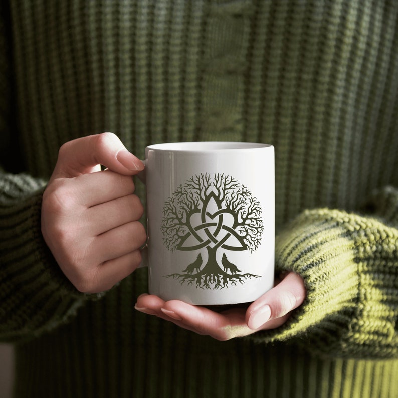 May include: White ceramic mug with a black and white design of a tree with a Celtic knot and two wolves. The tree is stylized with a heart shape at the center.