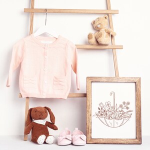 May include: A pink knitted cardigan hanging on a wooden ladder with a brown teddy bear, a brown bunny, and a framed print of a floral umbrella.
