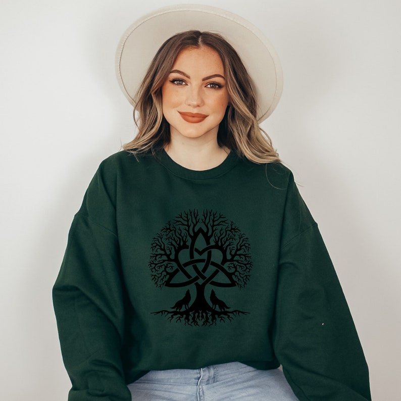 May include: A dark green sweatshirt with a black Celtic knot tree of life design. The tree has a large knot in the center and is surrounded by branches and roots.