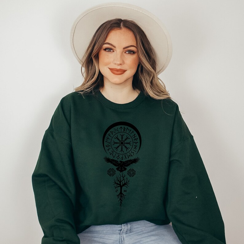May include: A dark green sweatshirt with a black graphic print of a Viking symbol, a bird, and a tree. The symbol is surrounded by runes.