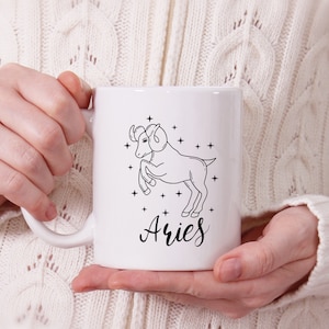 May include: White ceramic mug with a black line drawing of an Aries zodiac sign and the word "Aries" in cursive.