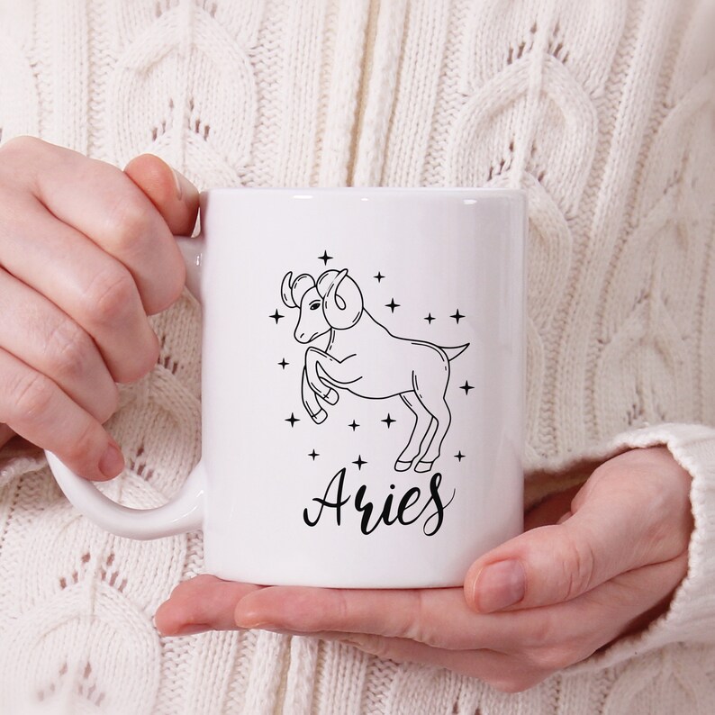 May include: White ceramic mug with a black line drawing of an Aries zodiac sign and the word "Aries" in cursive.