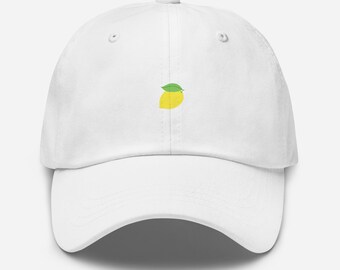 Può includere: Cappellino da baseball bianco con grafica di limone giallo e foglia verde. Il cappellino ha una visiera curva e un cinturino regolabile sul retro. Il design del limone è centrato sul davanti.