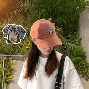 Könnte beinhalten: Eine Person trägt eine hellorange Baseballkappe mit einem gestickten Dackel-Design. Die Kappe hat einen gebogenen Schirm und einen schwarzen Riemen.