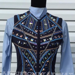 May include: A black sleeveless vest with a geometric design featuring blue, gold, and iridescent rhinestones. The vest has a zipper closure and is worn over a light blue shirt.