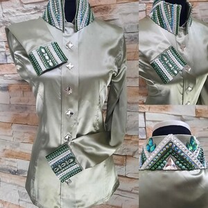 Peut inclure: Une chemise en satin vert sauge &agrave; col montant et manches longues. Le col et les poignets sont orn&eacute;s de strass verts et blancs. La chemise a une fermeture boutonn&eacute;e &agrave; l'avant.