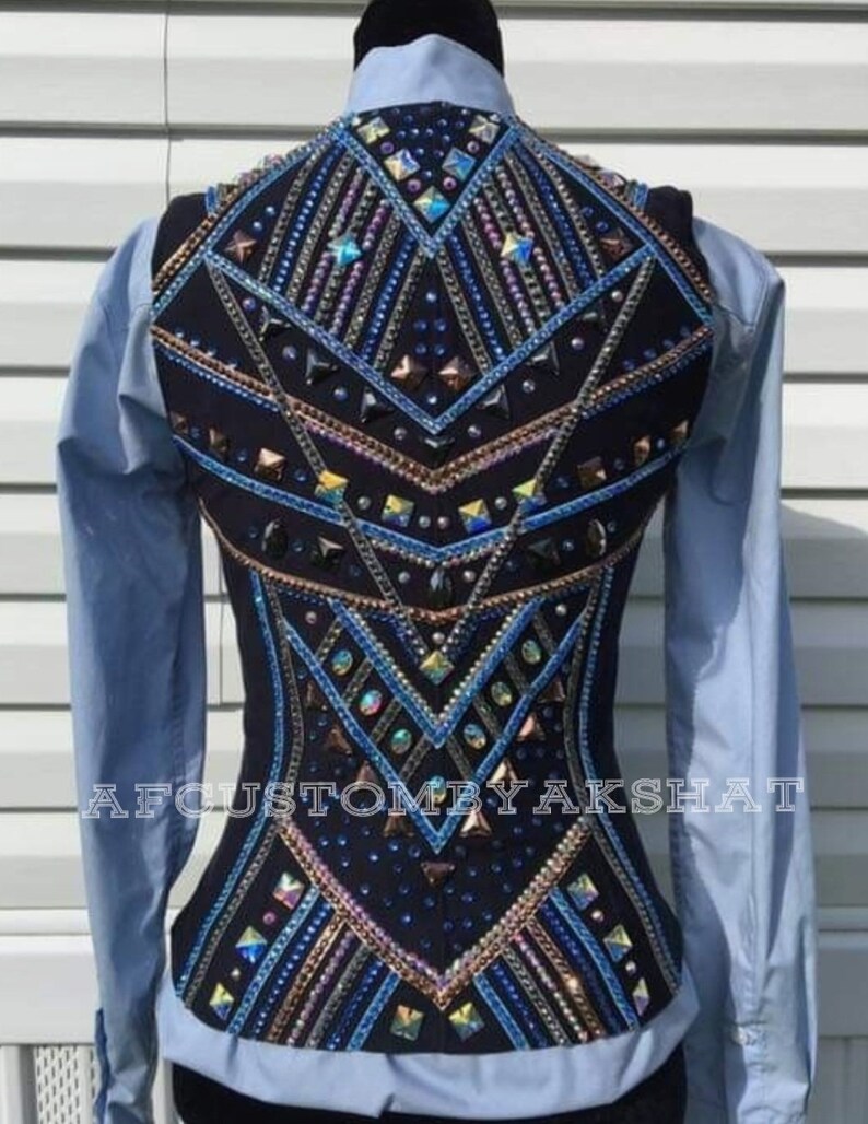 May include: A black show vest with a geometric design featuring blue, gold, and silver rhinestones. The vest has a fitted silhouette and a high back. The text "AFCUSTOMBYAKSHAT" is printed on the bottom of the vest.