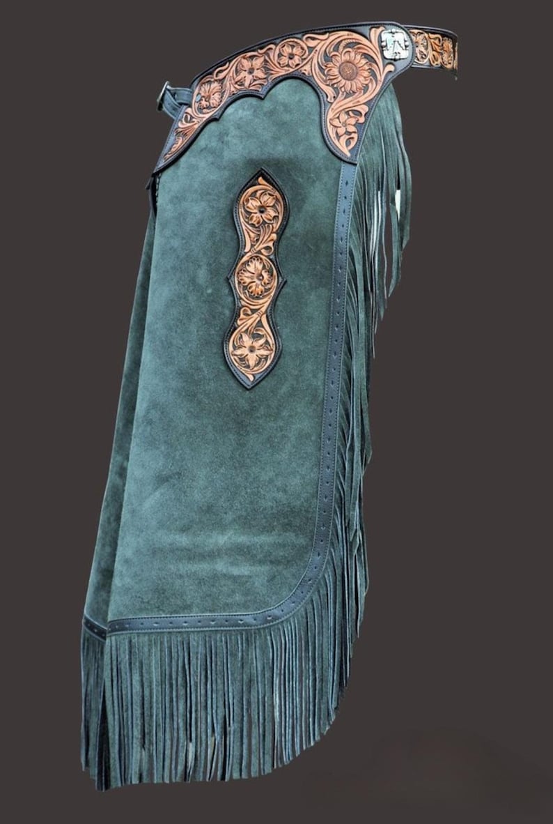 May include: Green suede chaps with decorative floral leather accents. The chaps feature a fringed hem and a detailed leather belt. The leather accents are brown with floral patterns.