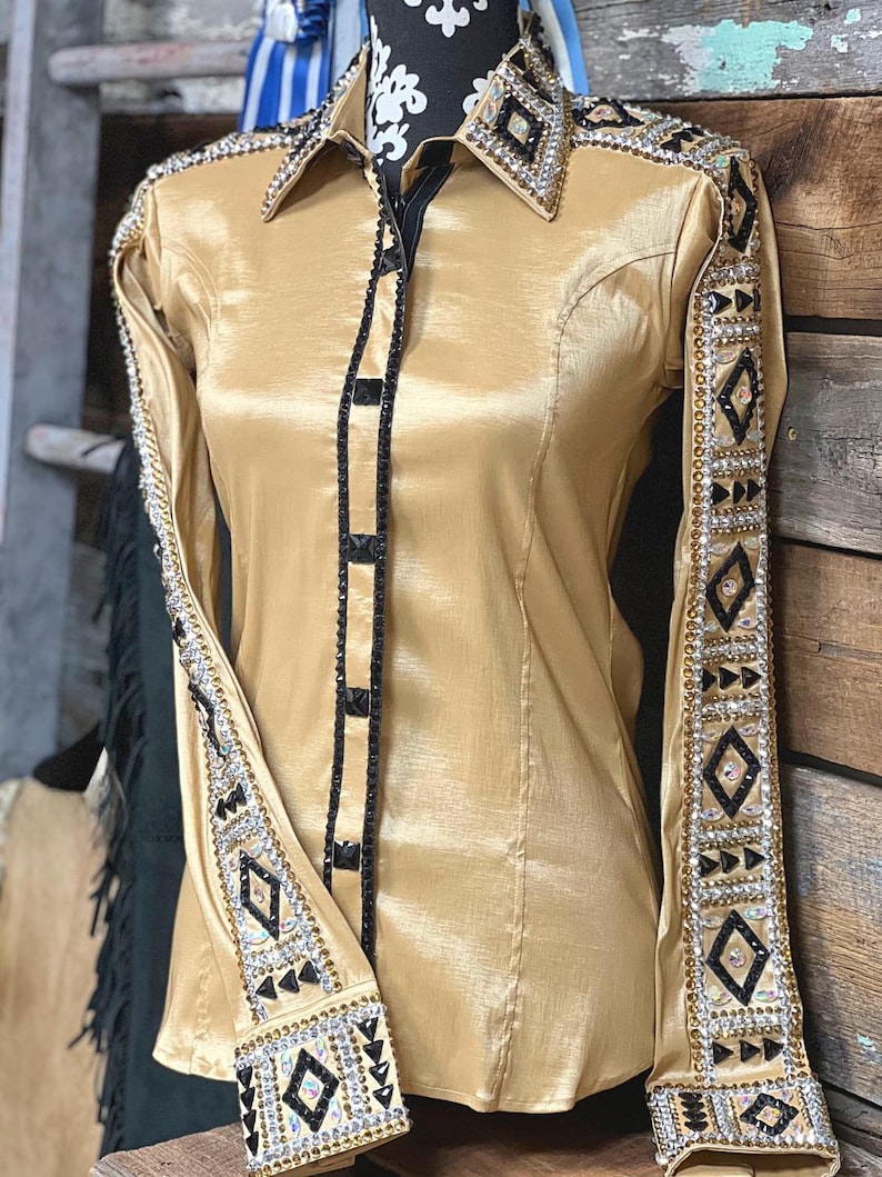 May include: A gold satin long-sleeve shirt with black trim and rhinestones. The shirt has a geometric pattern on the sleeves and collar.