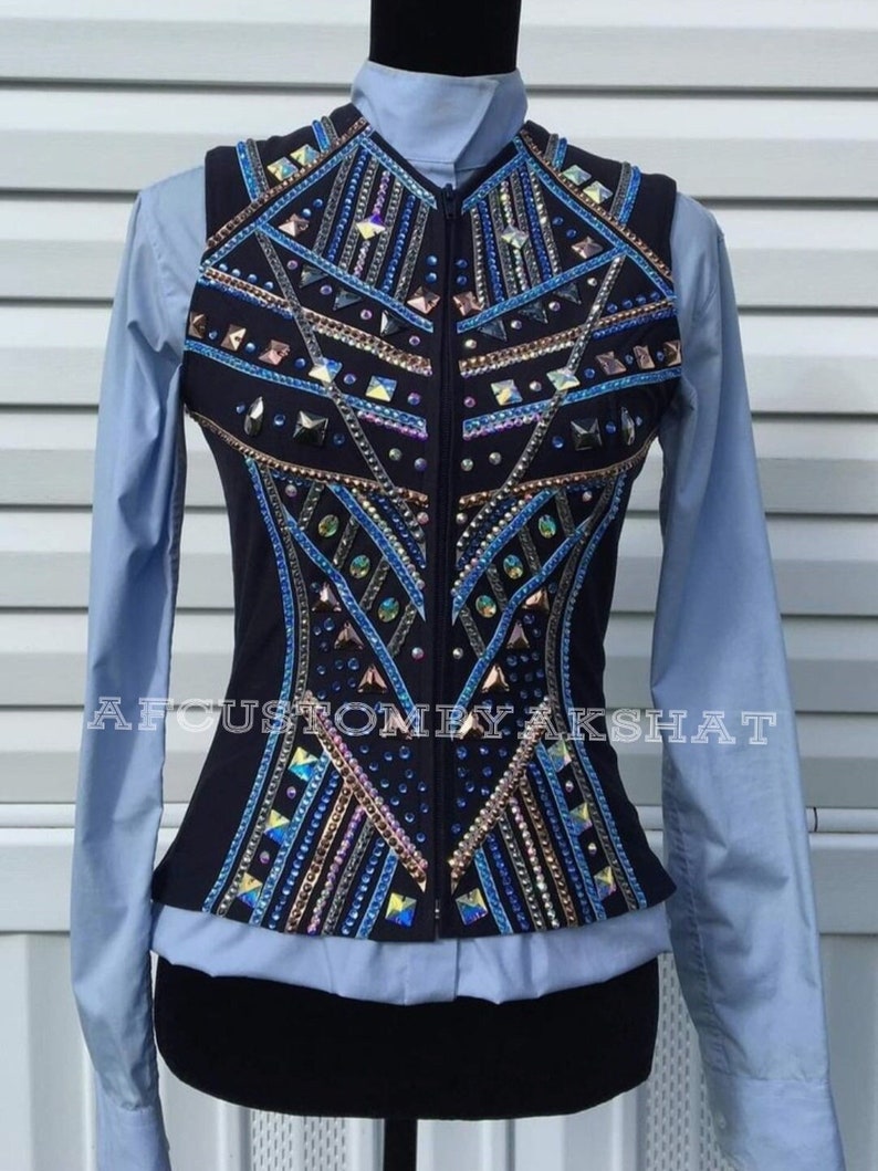 May include: A black sleeveless vest with a geometric design featuring blue, gold, and iridescent rhinestones. The vest has a zipper closure and is worn over a light blue shirt.