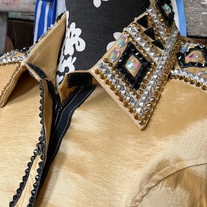May include: A gold satin shirt with a black zipper and a black and gold embellished collar. The collar features rhinestones and geometric shapes.