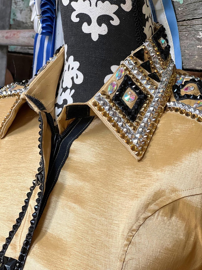 May include: A gold satin shirt with a black zipper and a black and gold embellished collar. The collar features rhinestones and geometric shapes.