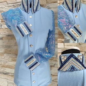 Peut inclure: Une chemise bleu clair avec une superposition de dentelle sur les manches. Le col et les poignets sont orn&eacute;s de strass et de bordures bleues.