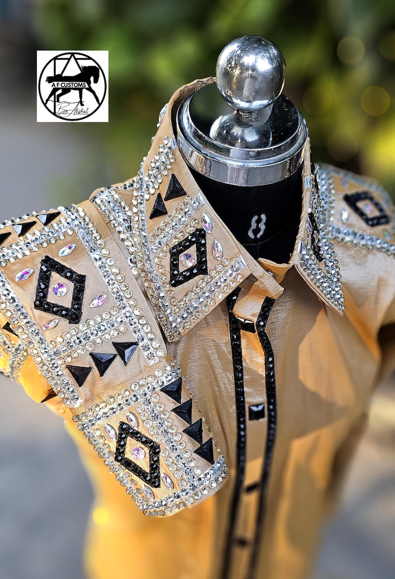 May include: A gold show shirt with black and silver embellishments. The shirt has a geometric pattern with rhinestones and black accents. The shirt is on a mannequin.
