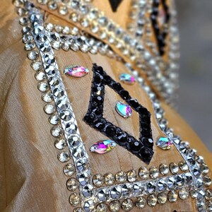 May include: A gold fabric show shirt with black and white geometric designs and rhinestones. The shirt has a black trim and a black and white diamond pattern.