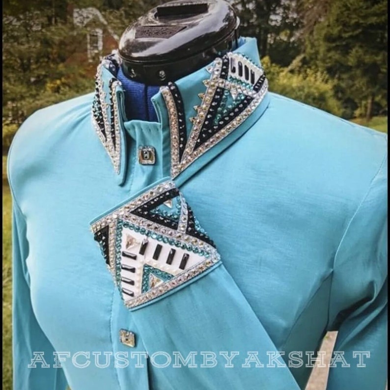 May include: A turquoise long-sleeve shirt with a black, white, and teal geometric design on the collar and cuffs. The design features rhinestones and is accented with black piping. The shirt is labeled "AFCUSTOMBYAKSHAT".