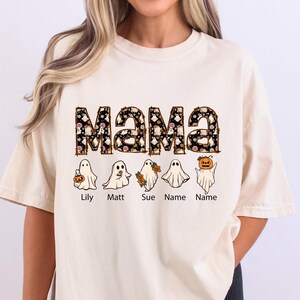 May include: A cream coloured t-shirt with the word "MAMA" in black and white with a Halloween themed pattern. The word "MAMA" is surrounded by five ghosts, each with a name underneath: Lily, Matt, Sue, Name, Name.