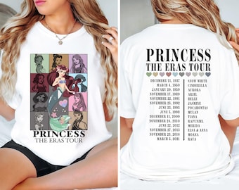 Pode incluir: Camiseta branca com um gráfico de princesas Disney em um padrão de grade. O texto "Princess The Eras Tour" é impresso abaixo do gráfico. A parte de trás da camiseta tem uma lista de princesas Disney e suas datas de lançamento.