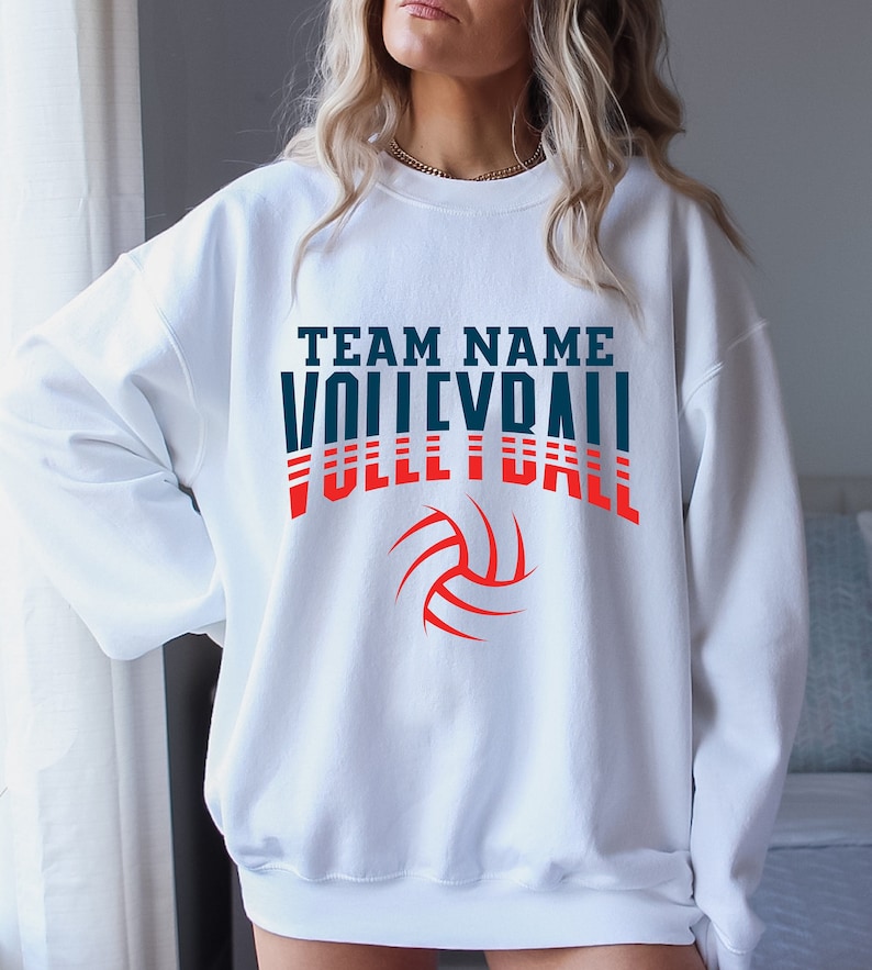 May include: White sweatshirt with the text "TEAM NAME VOLLEYBALL" in blue and red letters with a red volleyball graphic.