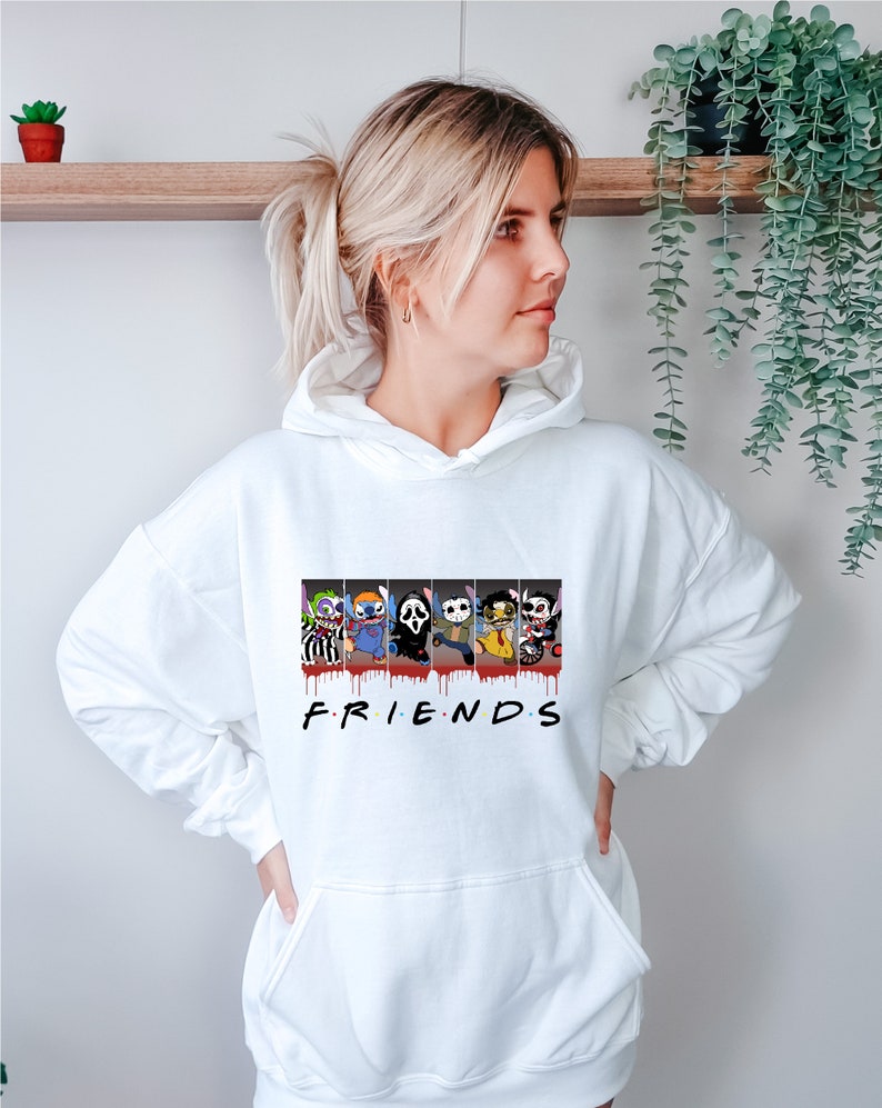 Op de afbeelding: Witte hoodie met een afbeelding van horrorfilmfiguren in een "Friends"-stijl ontwerp. De personages zijn Stitch, Ghostface, Jason Voorhees, Freddy Krueger en Michael Myers. De tekst "FRIENDS" is onder de afbeelding gedrukt.