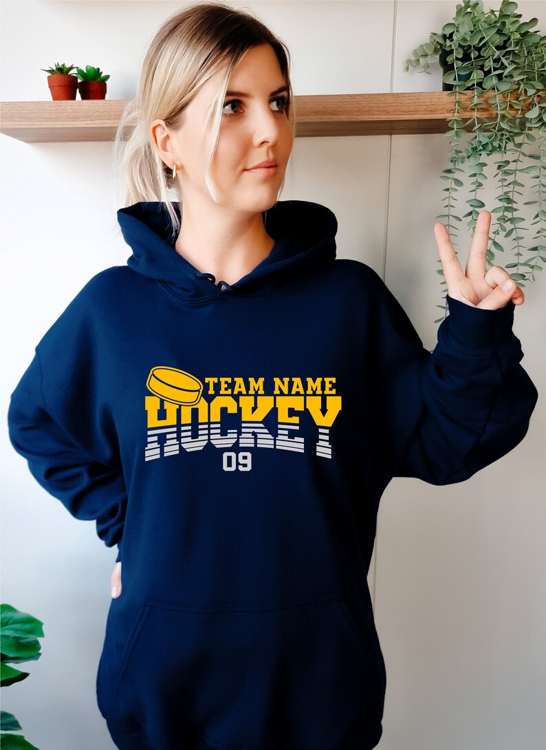 Może przedstawiać: Bordowa bluza z kapturem z ż&oacute;łto-białym nadrukiem z napisem "TEAM NAME HOCKEY 09".