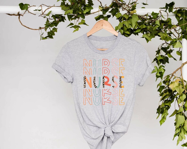 May include: A gray t-shirt with the word "NURSE" printed in colorful letters with a leopard print pattern. The letters are stacked on top of each other and are repeated multiple times.
