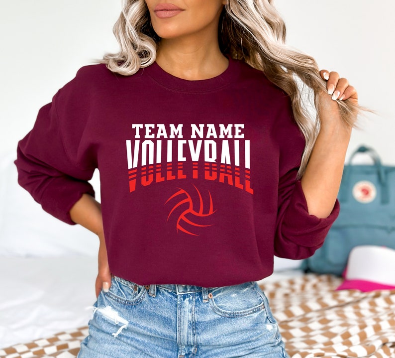 May include: Burgundy sweatshirt with white text that reads "TEAM NAME VOLLEYBALL" with a red volleyball graphic.