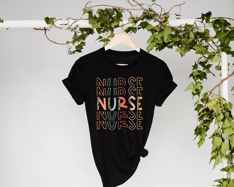 May include: A black t-shirt with the word 'NURSE' printed on it in a rainbow of colors. The word is repeated five times, with each repetition slightly offset from the one above it. The word 'NURSE' is also printed in a leopard print pattern in the center of the design.