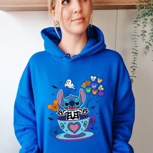 May include: A royal blue hoodie with a graphic of Stitch dressed as a skeleton holding balloons with Disney characters on them. Stitch is sitting in a teacup with a heart on the side. The graphic is surrounded by bats, spiderwebs, and stars.