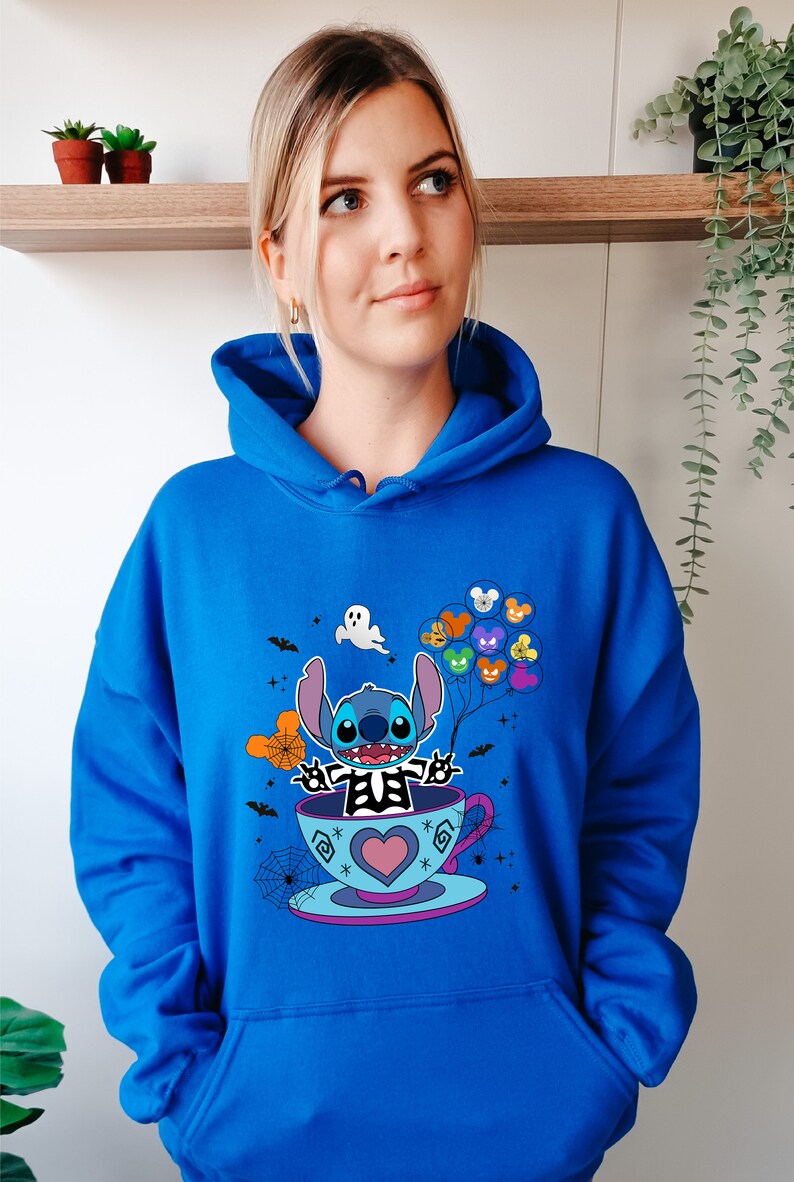 May include: A royal blue hoodie with a graphic of Stitch dressed as a skeleton holding balloons with Disney characters on them. Stitch is sitting in a teacup with a heart on the side. The graphic is surrounded by bats, spiderwebs, and stars.