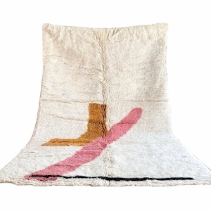 May include: A white rug with a geometric design in pink, orange, and black. The rug has a soft, fluffy texture.