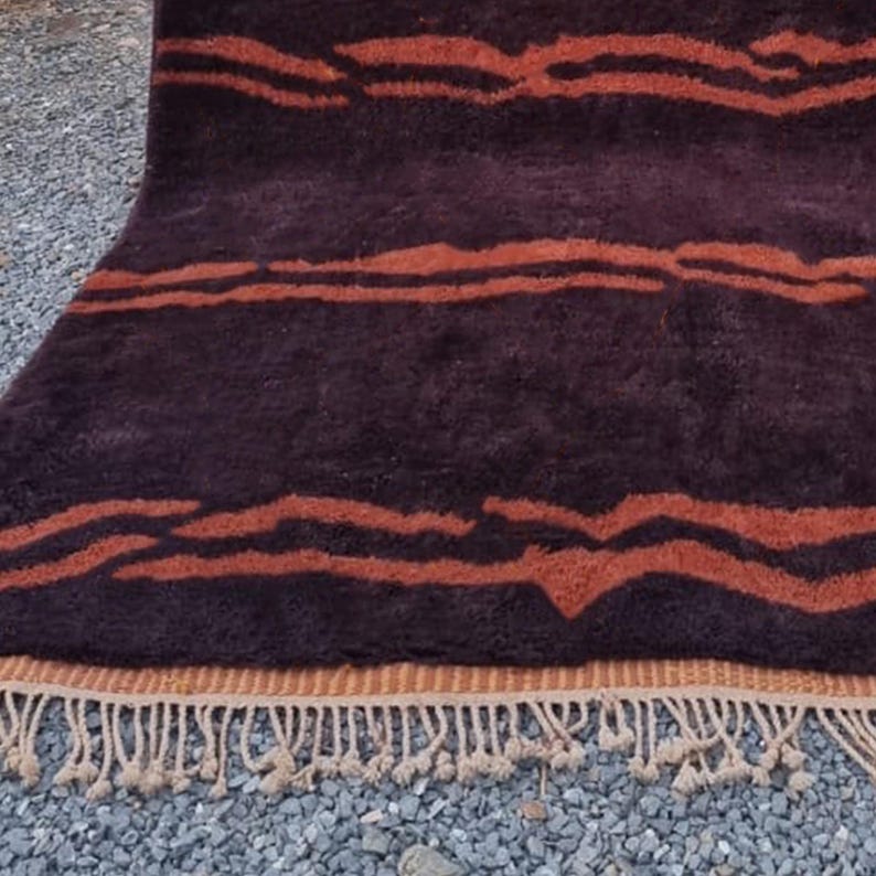 May include: A brown and orange striped rug with a fringe border. The rug has a wavy pattern and is made of a soft, plush material.