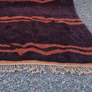 May include: A brown and orange striped rug with a fringe border. The rug has a wavy pattern and is made of a soft, plush material.