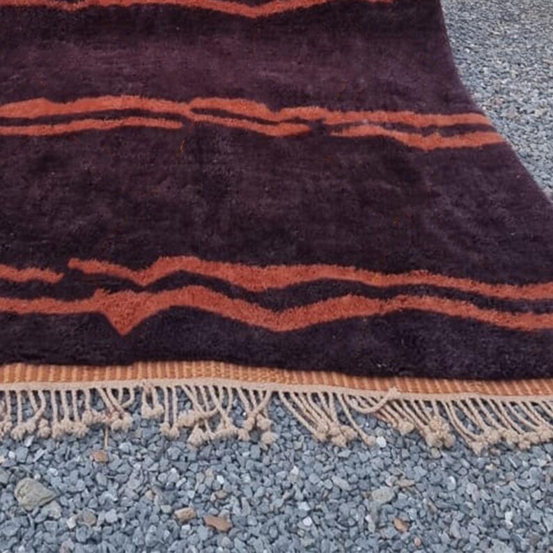 May include: A brown and orange striped rug with a fringe border. The rug has a wavy pattern and is made of a soft, plush material.