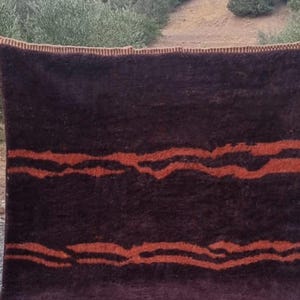 May include: A dark brown rug with a woven design of orange wavy lines. The rug has a fringe border.