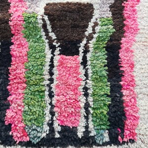 May include: Close-up of a colorful Moroccan rug with a geometric pattern in shades of pink, green, black, and white.