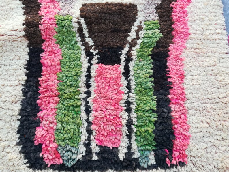 May include: Close-up of a colorful Moroccan rug with a geometric pattern in shades of pink, green, black, and white.