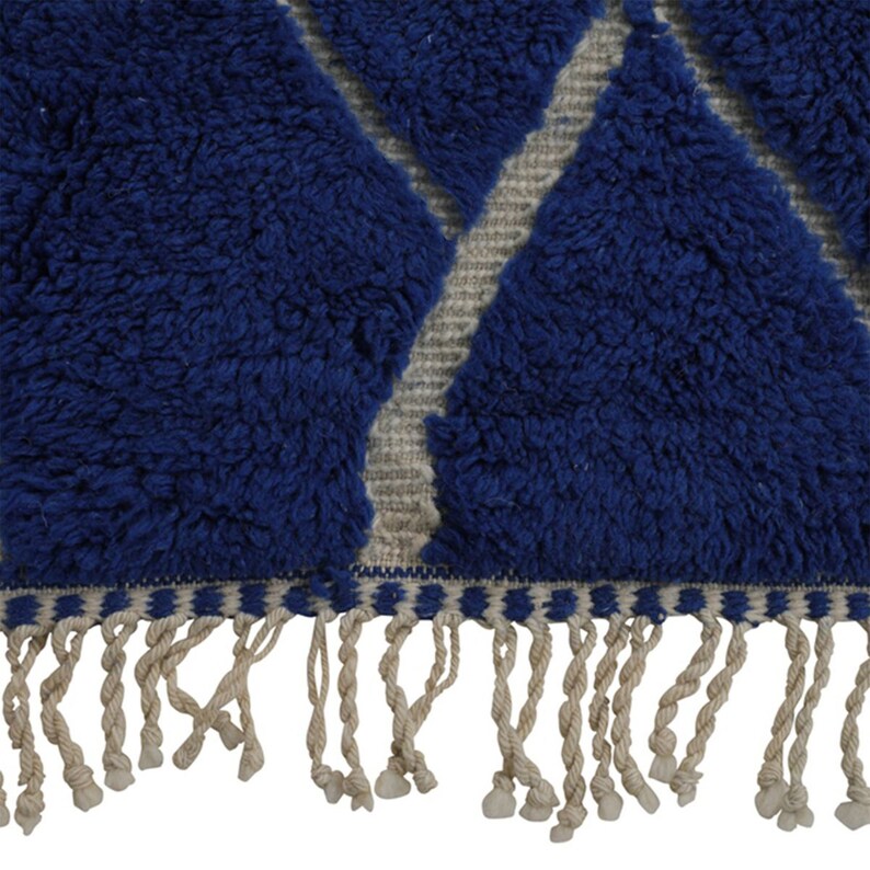 May include: Blue and white geometric patterned rug with a fringe border. The rug has a fluffy texture.