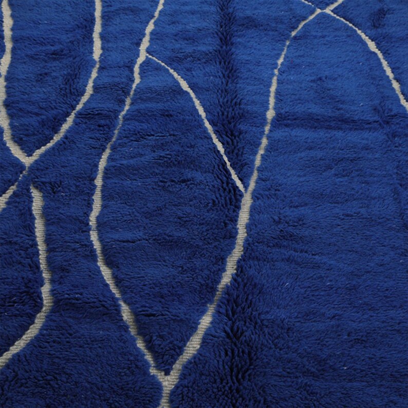 May include: Blue shag rug with a white abstract design. The design features curved lines and shapes.