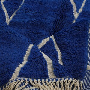 May include: A blue and white patterned rug with a fringe border. The rug has a fluffy texture and a geometric design.