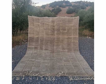 Puede incluir: Una alfombra grande, rectangular, de color beige con un patrón tejido. La alfombra tiene un borde de flecos y está sobre una superficie de grava.