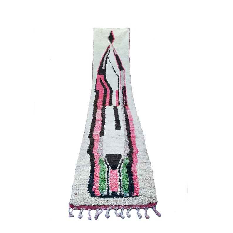 May include: A long, white rug with a geometric design in pink, black, and green. The rug has a fringe on the bottom.