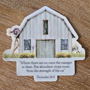 May include: A barn-shaped sticker with a watercolor illustration. The barn is white with a gray roof, green windows, and a large door. A windmill and text that reads "Where there are no oxen the manger is clean. But abundant crops come from the strength of the ox" are also included.